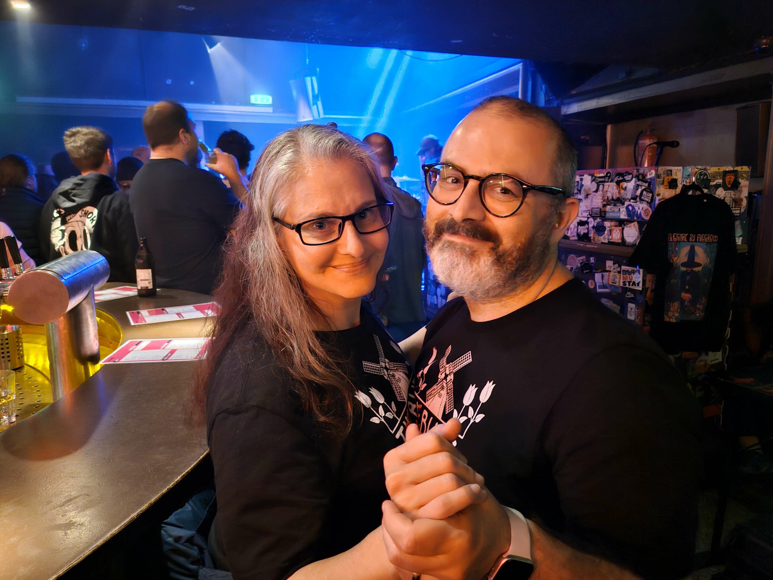 Debbie e Piermario abbracciati si tengono per mano soddidendo. Sono all'interno di un locale in cui si tiene un concerto rock