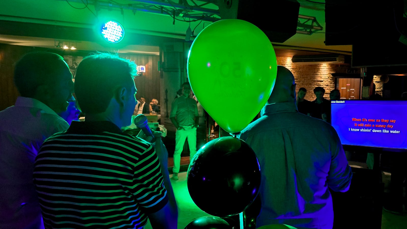 tre amici cantano durante una festa di compleanno in un locale illuminato da luci colorate